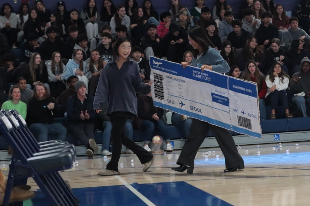 Branham student and her mother walk, holding a large plane ticket to Seoul, South Korea.
